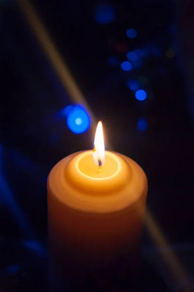 Vor dem Hintergrund einer Girlande mit leuchtenden Lichtern brennt eine große Kerze. Vertikales Foto, Defokus. Mystische esoterische Romanze Weissagung Stimmung Taufe Weihnachtslieder Setzer. — Stockfoto