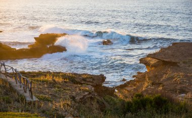 Gün batımında kayalara çarpan dalgalar.