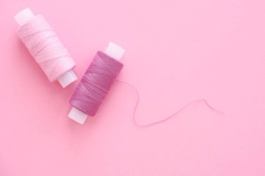 Pembe bir kağıt backgroun üzerinde dikiş iplik leylak (pembe, menekşe, kırmızı) iki makara, metin için alan kopyalamak. Üst görünüm, düz yatıyordu.