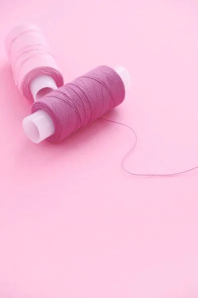 Close-up twee spoelen van naaigarens Lila (roze, Violet, Crimson) op een roze papieren backgroun, kopieer ruimte voor tekst. — Stockfoto