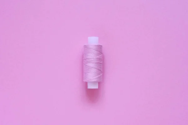 Een spoel van lila (roze, Violet, Crimson) naaien draad op een roze papier backgroun, kopieer ruimte voor tekst. Bovenaanzicht, vlakke lay. — Stockfoto