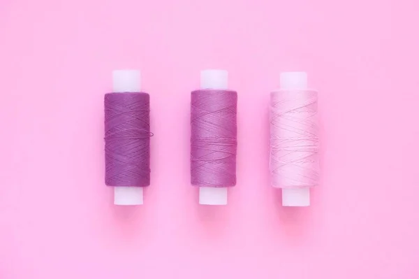Sewing thread kit of lilac (pink, violet, crimson) sewing thread on a pink paper backgroun, copy space for text. Top view, flat lay.