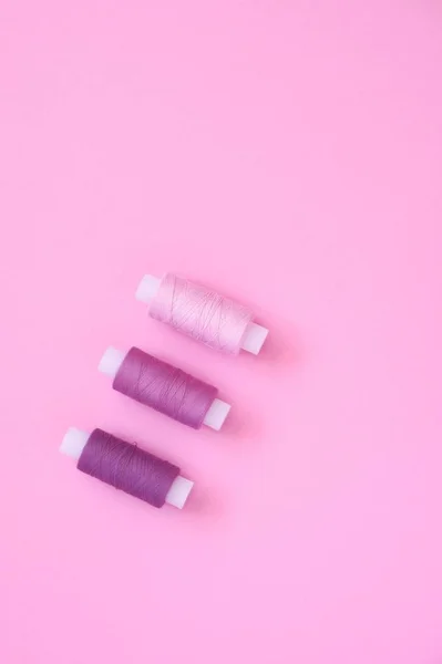 Naaigarens Kit van lila (roze, Violet, Crimson) naaigarens op een roze papieren backgroun, kopieer ruimte voor tekst. Bovenaanzicht, vlakke lay. — Stockfoto
