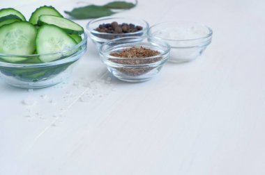 Cam bir kapta dilimlenmiş taze bir salatalığın yakın çekimve turşu (fermantasyon)- dereotu tohumu, biber, beyaz ahşap bir masada tuz için gerekli baharatlar. Seçici odaklama, metin için kopya alanı.