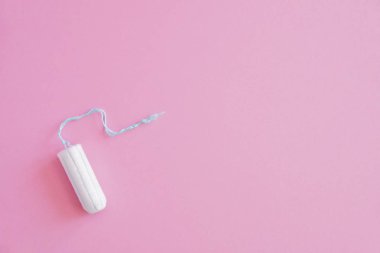 Pembe arka planda hijyenik bir tampon. Menstrüel güve döngüsü, korunma aracı. Üst görünüm, düz döşeme, metin için kopyalama alanı.
