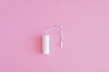 Pembe arka planda hijyenik bir tampon. Menstrüel güve döngüsü, korunma aracı. Üst görünüm, düz döşeme, metin için kopyalama alanı.