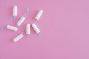 Pembe arka planda birkaç beyaz hijyenik tampon. Menstrüel güve döngüsü, korunma aracı. Üst görünüm, düz döşeme, metin için kopyalama alanı.