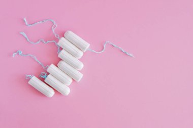 Pembe arka planda birkaç beyaz hijyenik tampon. Menstrüel güve döngüsü, korunma aracı. Üst görünüm, düz döşeme, metin için kopyalama alanı.