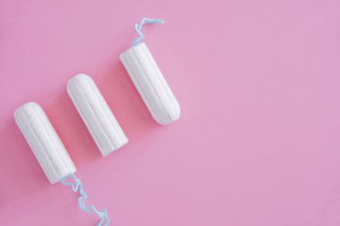 Pembe arka planda üç hijyenik tampon. Menstrüel güve döngüsü, korunma aracı. Üst görünüm, düz döşeme, metin için kopyalama alanı.