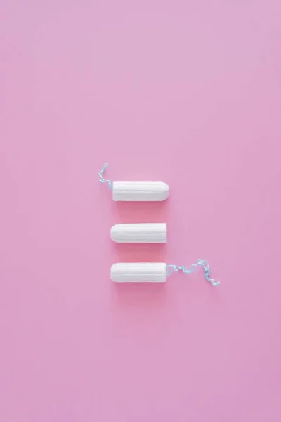 Pembe arka planda üç hijyenik tampon. Menstrüel güve döngüsü, korunma aracı. Üst görünüm, düz döşeme, metin için kopyalama alanı.