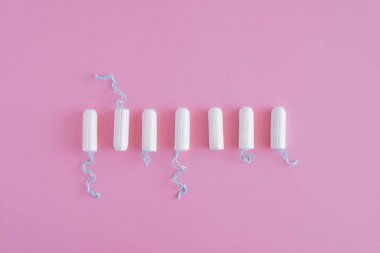Pembe arka planda birkaç beyaz hijyenik tampon. Menstrüel güve döngüsü, korunma aracı. Üst görünüm, düz döşeme, metin için kopyalama alanı.