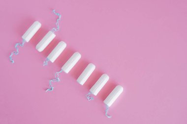 Pembe arka planda birkaç beyaz hijyenik tampon. Menstrüel güve döngüsü, korunma aracı. Üst görünüm, düz döşeme, metin için kopyalama alanı.
