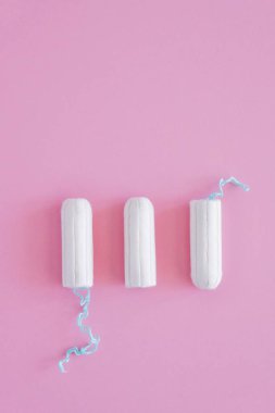 Pembe arka planda üç hijyenik tampon. Menstrüel güve döngüsü, korunma aracı. Üst görünüm, düz döşeme, metin için kopyalama alanı.