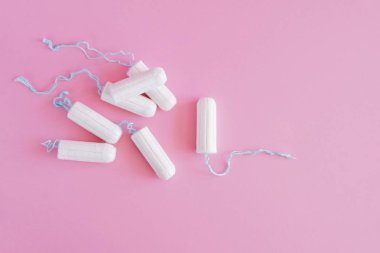 Pembe arka planda birkaç beyaz hijyenik tampon. Menstrüel güve döngüsü, korunma aracı. Üst görünüm, düz döşeme, metin için kopyalama alanı.