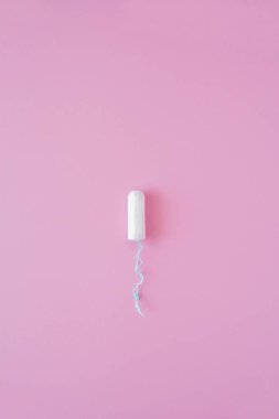 Pembe arka planda hijyenik bir tampon. Menstrüel güve döngüsü, korunma aracı. Üst görünüm, düz döşeme, metin için kopyalama alanı.