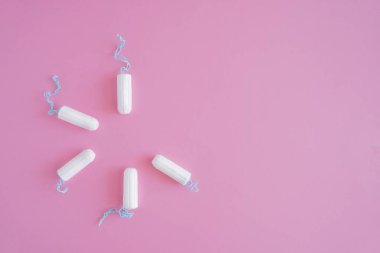 Pembe arka planda birkaç beyaz hijyenik tampon. Menstrüel güve döngüsü, korunma aracı. Üst görünüm, düz döşeme, metin için kopyalama alanı.