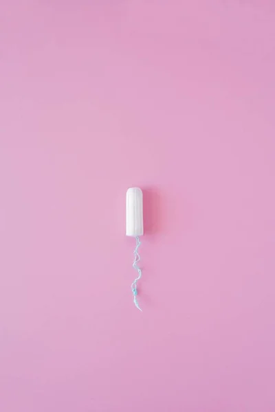 Pembe arka planda hijyenik bir tampon. Menstrüel güve döngüsü, korunma aracı. Üst görünüm, düz döşeme, metin için kopyalama alanı.