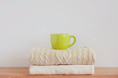 Sıcak bir içecek ile yeşil bir fincan (kahve, çay, kakao, kapuçino) düzgünce katlanmış örgü kazak bir yığın üzerinde bej arka plan üzerinde. Konfor, sıcaklık, rahatlık, sonbahar-kış sezonu kavramı.