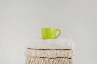 Sıcak bir içecek ile yeşil bir fincan (kahve, çay, kakao, kapuçino) düzgünce katlanmış örgü kazak bir yığın üzerinde bej arka plan üzerinde. Konfor, sıcaklık, rahatlık, sonbahar-kış sezonu kavramı.