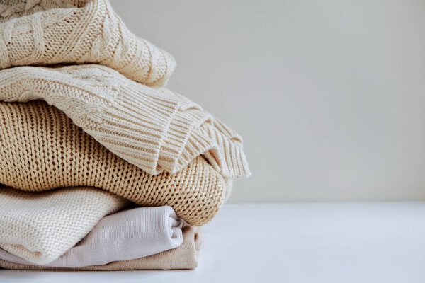Warm sweaters in a pile, knitted texture, minimalism lifestyle, capsule wardrobe, autumn-winter season. With selective focus and copy space.