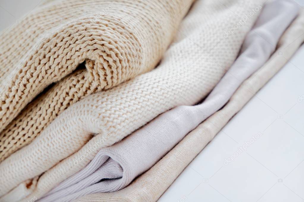 Warm sweaters in a pile, knitted texture, minimalism lifestyle, capsule wardrobe, autumn-winter season. With selective focus and copy space.