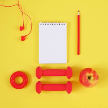Yaratıcı düz yatıyordu spor ve fitness konsepti. Dilsiz, kulaklık, el genişletici, elma, defter ve kalemin metin için alan içeren sarı arka plan üzerinde üst görünümü.