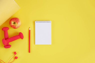 Yaratıcı düz yatıyordu spor ve fitness konsepti. Dilsiz, kulaklık, el genişletici, elma, defter ve kalemin metin için alan içeren sarı arka plan üzerinde üst görünümü.