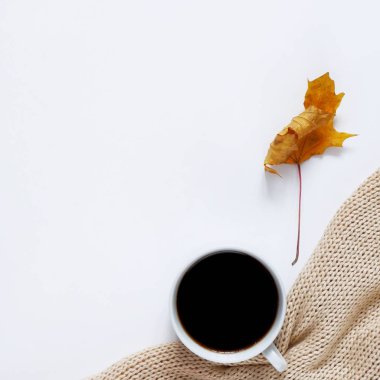 Bir fincan sıcak kahvenin sonbahar kompozisyonu, sıcak bir süveter ve beyaz arka planda sarı bir akçaağaç yaprağı. Üst görünüm, düz görünüm, metin için alanı kopyala.