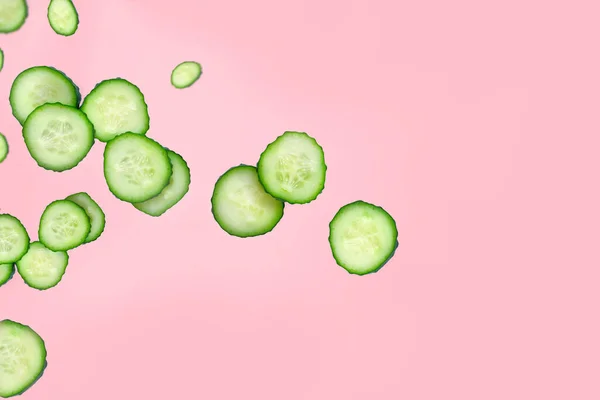 Flying green slices of fresh cut cucumber on a pink background. Vegetables pattern, flying food concept, green vegetables, diet food, blog food. Copy space for text.