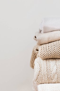 Güzelce katlanmış, bej arka planda yün süveter yığınını kapat. Kapsül dolabı, gardırop, minimalizm, örgü dokuma, düzen, konfor, makro. Metin için kopyalama alanı ile dikey.