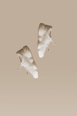 Bej arka planda uçan modern kadın spor ayakkabıları. Modaya uygun minimalizm, havaya yükselme ayakkabıları, yaratıcı düzen. Metin için kopyalama alanı ile dikey.