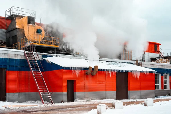 Industrial building, factory. Winter, icicles on the facade, steam from pipes