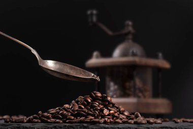 Kahve öğütücüsünün içinde kahve çekirdeklerinin yanında, taştan bir masanın üstünde. Kahve dolduran bir kaşık.