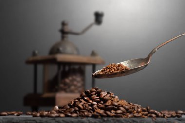 Kahve öğütücüsünün içinde kahve çekirdeklerinin yanında, taştan bir masanın üstünde. Kahve dolduran bir kaşık.