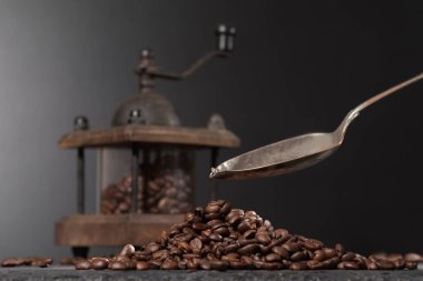 Kahve öğütücüsünün içinde kahve çekirdeklerinin yanında, taştan bir masanın üstünde. Kahve dolduran bir kaşık.