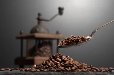 Kahve öğütücüsünün içinde kahve çekirdeklerinin yanında, taştan bir masanın üstünde. Kahve dolduran bir kaşık.