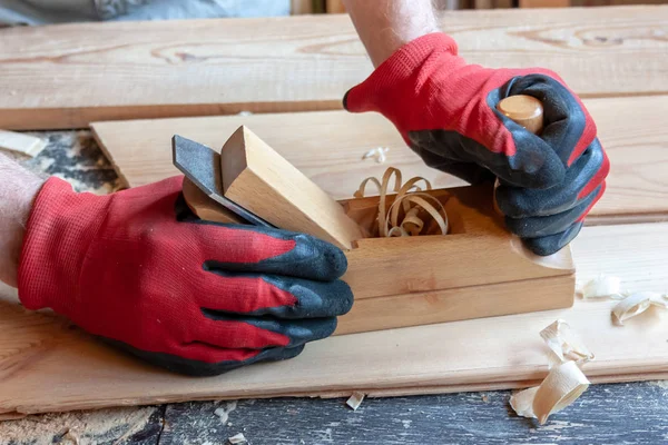 Um carpinteiro em luvas de pano vermelho segura um jointer de madeira em suas mãos — Fotografia de Stock