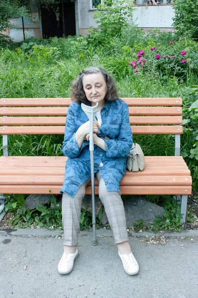 Evin yakınındaki bir bankta elinde koltuk değneği olan üzgün yaşlı bir kadın. Dikey fotoğraf