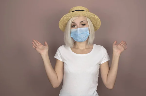 Hasır şapkalı beyaz saçlı güzel bir kız, beyaz tişört ve pembe arka planda koruyucu bir tıbbi maske, mesaj atmak için yer.