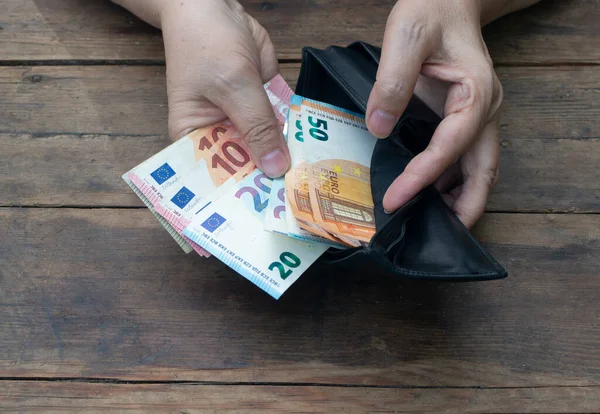 Eller, 10, 20, 50 avroluk banknotları tahtadan bir arka planda siyah bir cüzdana koydu. Yoksulluk veya zenginlik kavramı