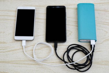 Masadaki mavi güç bankasından iki akıllı telefon, siyah-beyaz şarj ediliyor.