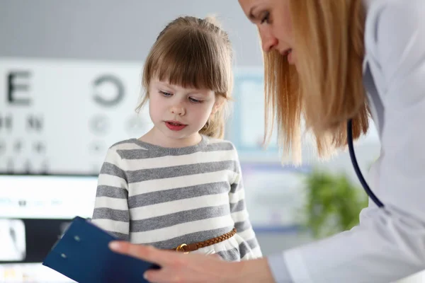 Femmina medico ascolto carino poco paziente e la scrittura di informazioni di registrazione sul blocco appunti — Foto Stock