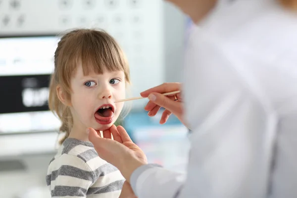 木製の棒で小さな子供の患者の喉を調べる女性小児科医 — ストック写真