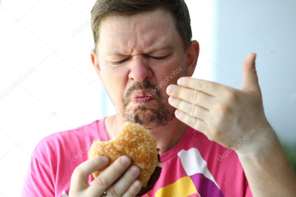 Unhappy man sniffing suspicious burger examining its freshness