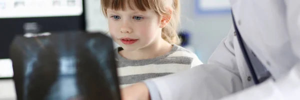 Menina bonito falando com gp olhando para imagem de raio-x durante a consulta — Fotografia de Stock