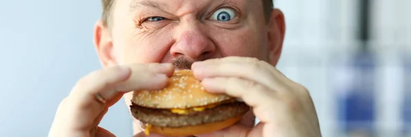 Aneh pria berjanggut dengan idiot ekspresi wajah makan burger besar — Stok Foto