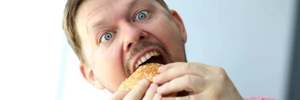 Смешной бородатый мужчина с идиотским выражением лица ест бургер — стоковое фото