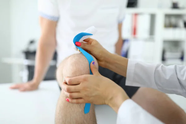 Doctor lijm kinesio tape aan de mens op zijn knie closeup — Stockfoto