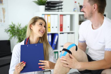 Kadın doktor hastanın bacağındaki Kinesio bandını sabitledi..