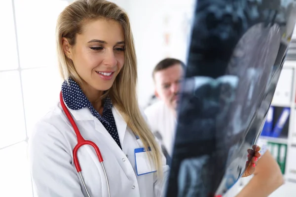 Mulher médico olha para uma imagem de raios X, juntamente com o paciente . — Fotografia de Stock
